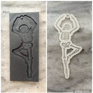 May include: A grey silicone mould of a skeleton in a yoga pose. The mould is on a grey textured surface. The skeleton is in a tree pose.