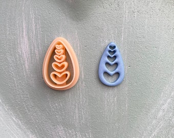 Könnte beinhalten: Zwei Ausstecher in Tropfenform mit einer Reihe von Herzen im Inneren. Der Ausstecher links ist beige und der Ausstecher rechts ist blau.