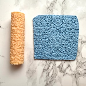 May include: Two silicone cake decorating tools. One is a light brown cylinder with a textured surface. The other is a light blue square with a textured surface.