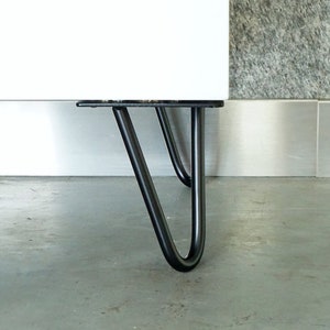 Op de afbeelding: Een wit kastje met zwarte haarspeldpoten. De poten zijn van metaal en hebben een eenvoudig, modern ontwerp.