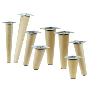 Puede incluir: Una colección de patas de muebles de madera de varios tamaños. Cada pata tiene un diseño cónico y está hecha de madera de color claro. Cuentan con una placa de montaje metálica cuadrada en la parte superior.