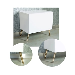 Op de afbeelding: Een witte kast met een gouden metalen basis. De kast heeft een eenvoudig ontwerp en is perfect om spullen in een slaapkamer, woonkamer of kantoor op te bergen.