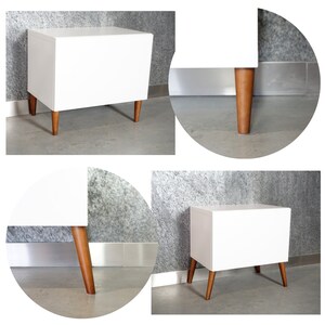 May include: White nightstand with four wooden legs. The nightstand has a simple, modern design.