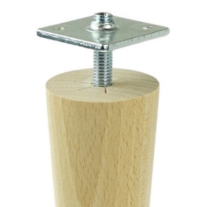 May include: A wooden furniture leg with a metal mounting plate and screw. The leg is light brown and has a tapered shape.