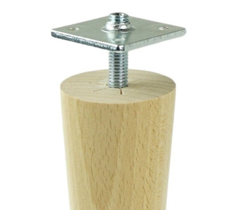 May include: A wooden furniture leg with a metal mounting plate and screw. The leg is light brown and has a tapered shape.