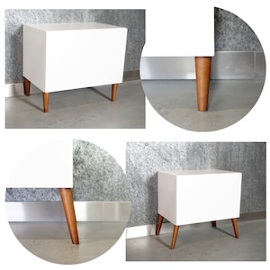 May include: White nightstand with four wooden legs. The nightstand has a simple, modern design.