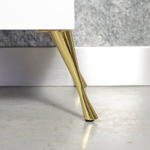 Może przedstawiać: Zbliżenie na białą szafkę z złotymi metalowymi nóżkami. Nóżki są zwężające się i mają zaokrągloną podstawę.