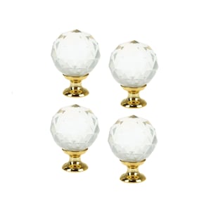 Könnte beinhalten: Satz mit vier klaren Kristall-Schrankknöpfen mit goldenen Sockeln. Jeder Knopf hat ein facettierendes Design.