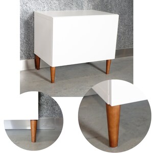 May include: White cabinet with a single drawer and four wooden legs. The cabinet is sitting on a gray floor.