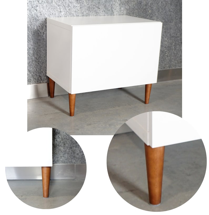 May include: White cabinet with a single drawer and four wooden legs. The cabinet is sitting on a gray floor.