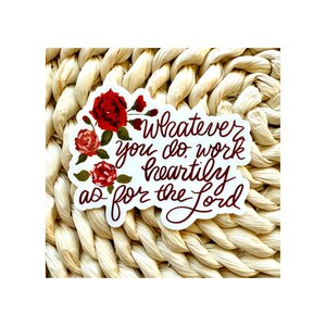 May include: A white sticker with red roses and green leaves. The sticker has the text "Whatever you do work heartily as for the Lord" in a handwritten style font. The sticker is on a woven background.