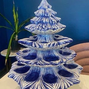 Könnte beinhalten: Ein mehrstöckiger Servierständer aus Keramik in Form eines Weihnachtsbaums. Der Ständer ist blau und weiß mit einem detaillierten, strukturierten Design. Er hat mehrere Ebenen mit kreisförmigen Vertiefungen. Der Sockel besteht aus silberfarbenem Metall. Ideal für Süßigkeiten.