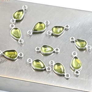 May include: A collection of small, teardrop-shaped charms featuring translucent light green gemstones encased in silver-toned metal settings. Each charm has two small circular loops on opposite ends, allowing for easy attachment to jewelry chains.