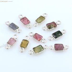 Può includere: Una collezione di dieci connettori rettangolari per gioielli, ciascuno caratterizzato da una piccola pietra preziosa multicolore incastonata in una cornice di metallo color argento con due anelli circolari alle estremità. Le pietre presentano varie tonalità.