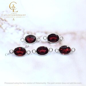 Pode incluir: Cinco pedras preciosas granada vermelho-escuras de formato oval em molduras de metal prateado. Cada pe&ccedil;a apresenta uma superf&iacute;cie facetada e dois pequenos elos circulares nos lados opostos. O texto CATLISTNMINIMALIST GEMSTONE & JEWELRY &eacute; vis&iacute;vel.