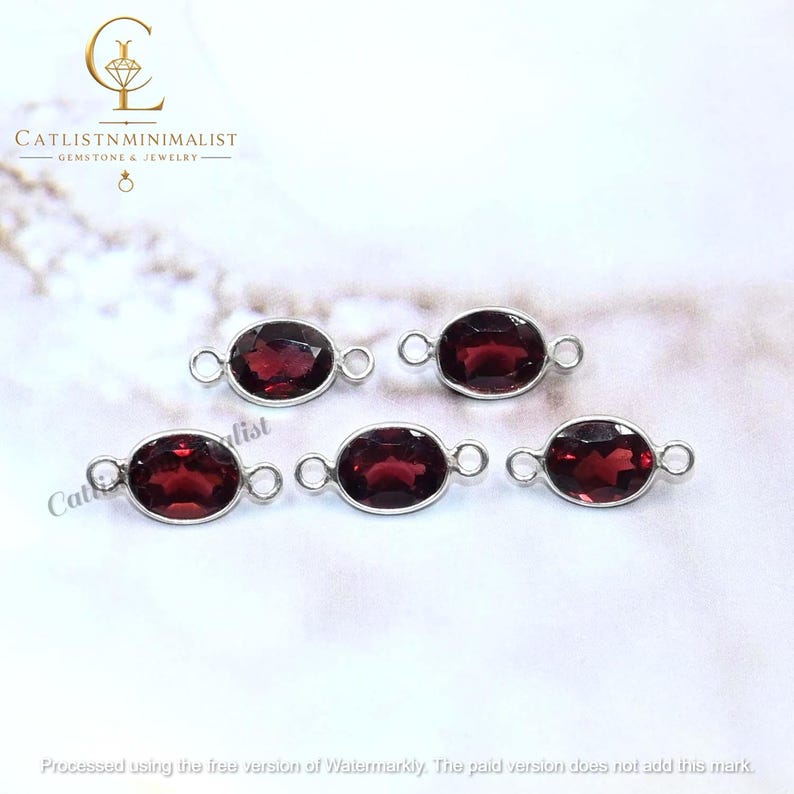 Pode incluir: Cinco pedras preciosas granada vermelho-escuras de formato oval em molduras de metal prateado. Cada pe&ccedil;a apresenta uma superf&iacute;cie facetada e dois pequenos elos circulares nos lados opostos. O texto CATLISTNMINIMALIST GEMSTONE & JEWELRY &eacute; vis&iacute;vel.