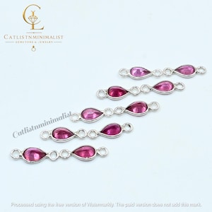 May include: A collection of silver-toned jewelry connectors featuring small, teardrop-shaped magenta gemstones. Each connector has a metal loop on both ends. The image includes the text CATLISTNMINIMALIST GEMSTONE & JEWELRY and a watermark.
