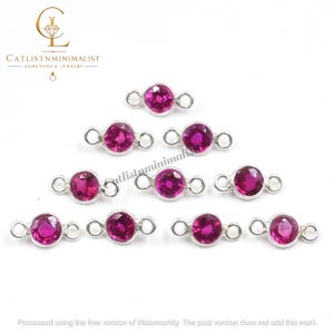 May include: A collection of nine silver-toned jewelry connectors, each featuring a circular, faceted, vibrant pink gemstone set in a metal bezel with a small loop on either side for attachment, arranged in a staggered formation on a white background.