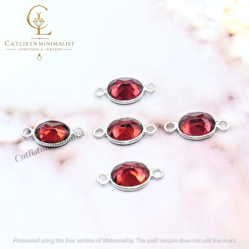 Pode incluir: Cinco conectores de joias ovais com pedras preciosas vermelho-escuras facetadas em arma&ccedil;&otilde;es de metal prateado. Cada conector possui um pequeno la&ccedil;o circular em ambas as extremidades para fixa&ccedil;&atilde;o, com um acabamento polido e tom vermelho.