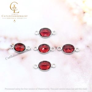 Pode incluir: Quatro conectores de joias de formato oval com pedras preciosas vermelho-escuras facetadas em molduras de metal prateado. Cada conector possui dois pequenos aros circulares nos lados opostos. O logotipo CATLISTNMINIMALIST &eacute; vis&iacute;vel.