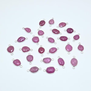 Könnte beinhalten: Eine Sammlung von 25 rosafarbenen Edelstein-Verbindungsanhängern mit silberfarbenen Sprungringen. Die Edelsteine sind oval geformt und haben eine facettierte Oberfläche.