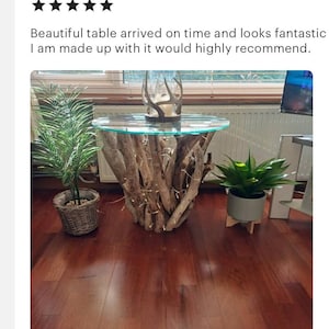 May include: A round glass-top table with a unique base made of driftwood branches. The table is in a room with hardwood floors and features a decorative antler centerpiece.