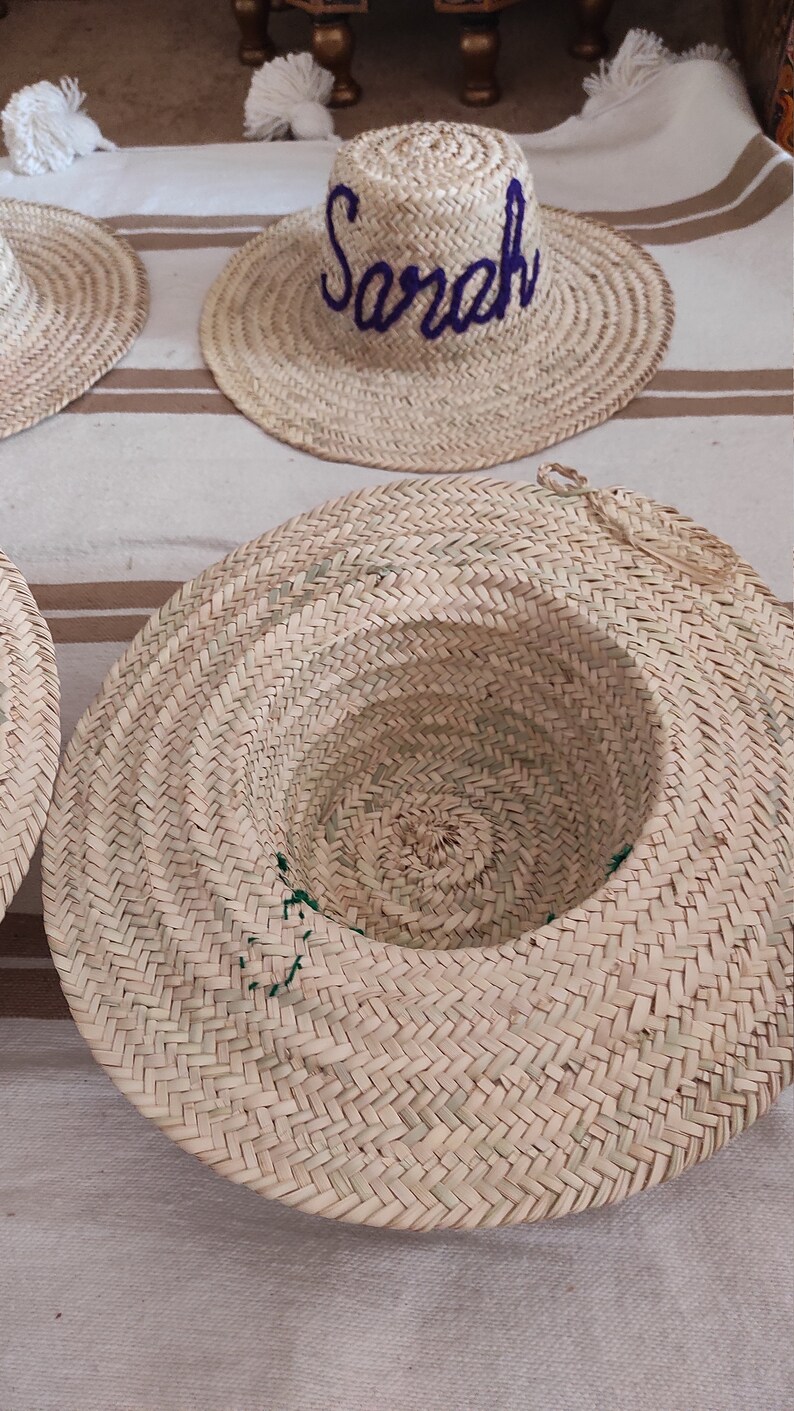 May include: A straw hat with a purple embroidered name "Sarah" on the front. The hat is woven with a herringbone pattern.