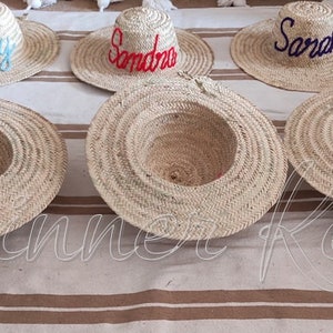 May include: Five straw hats with different names embroidered on them. The names are Ruby, Sandra, Sarah, and two blank hats.