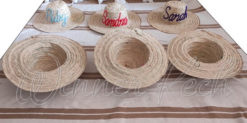 May include: Five straw hats with different names embroidered on them. The names are Ruby, Sandra, Sarah, and two blank hats.