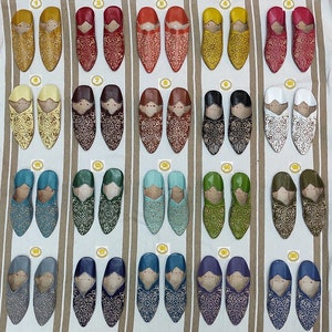 K&ouml;nnte beinhalten: Zwanzig Paar Lederschlappen mit aufwendigen Stickereien in verschiedenen Farben, darunter Gelb, Rot, Braun, Wei&szlig;, Blau, Gr&uuml;n und Lila. Die Schlappen sind in Reihen auf einem gestreiften Stoffhintergrund angeordnet.