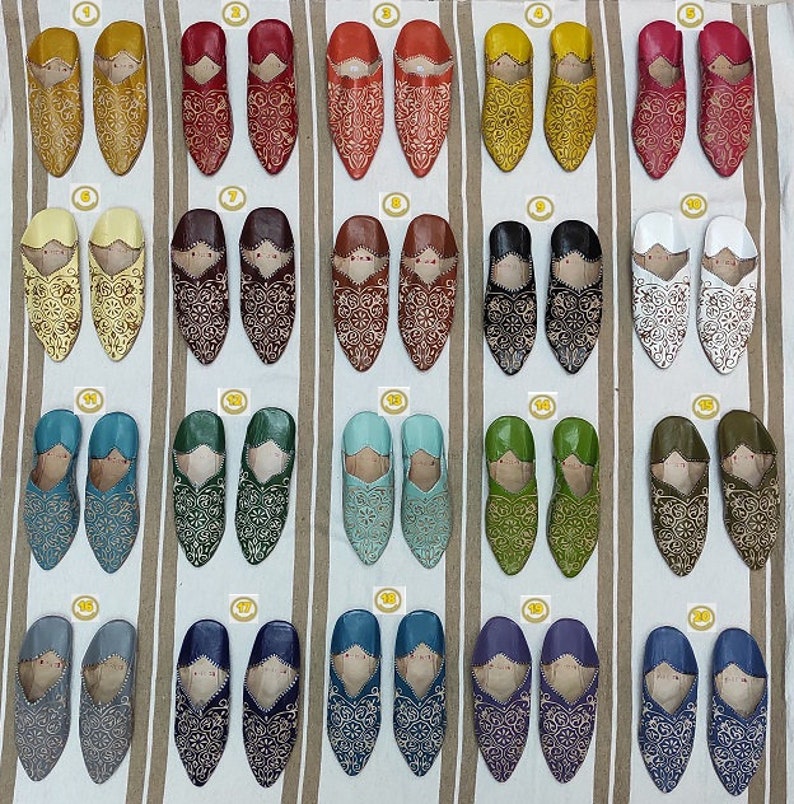 K&ouml;nnte beinhalten: Zwanzig Paar Lederschlappen mit aufwendigen Stickereien in verschiedenen Farben, darunter Gelb, Rot, Braun, Wei&szlig;, Blau, Gr&uuml;n und Lila. Die Schlappen sind in Reihen auf einem gestreiften Stoffhintergrund angeordnet.
