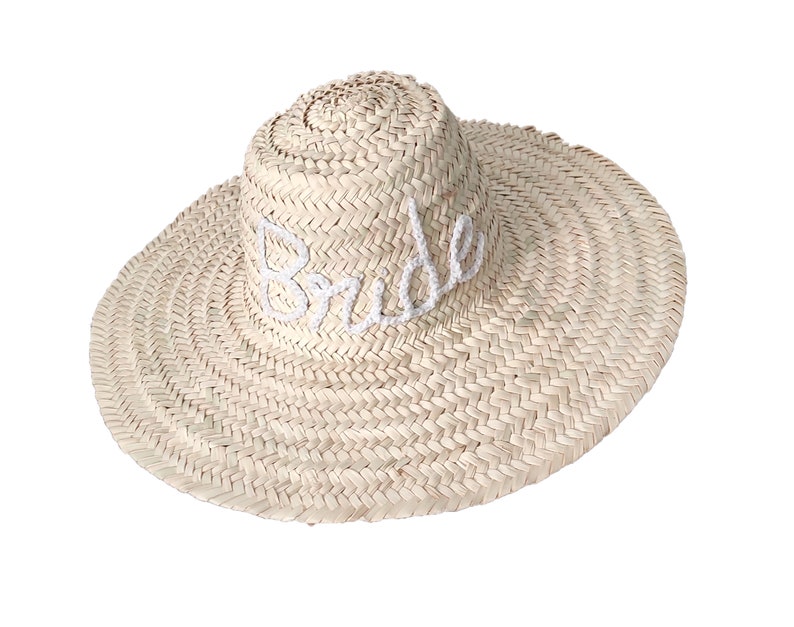 May include: A straw sun hat with a wide brim and the word "Bride" embroidered in white on the front.