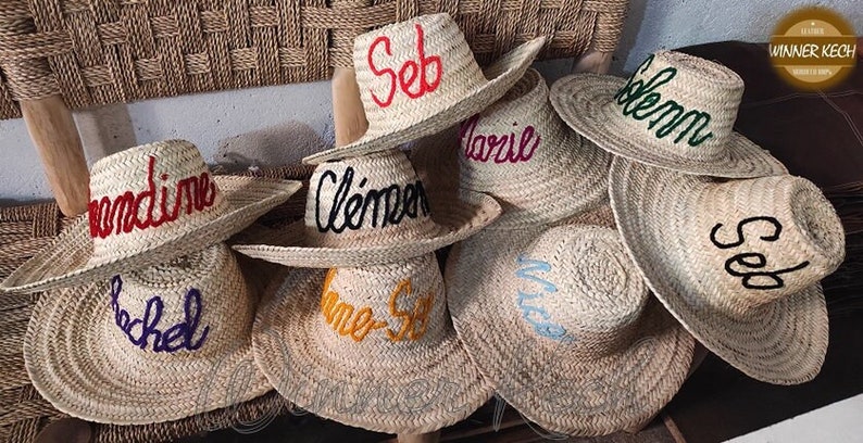 May include: A collection of straw hats with different colored embroidery. The hats are personalized with names like "Seb", "Clemence", "Marlie", "Noemie", "Rachel", "Winner Keech", and "Solemn".