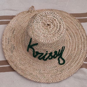May include: A straw hat with a green embroidered word "Kristy" on the front.