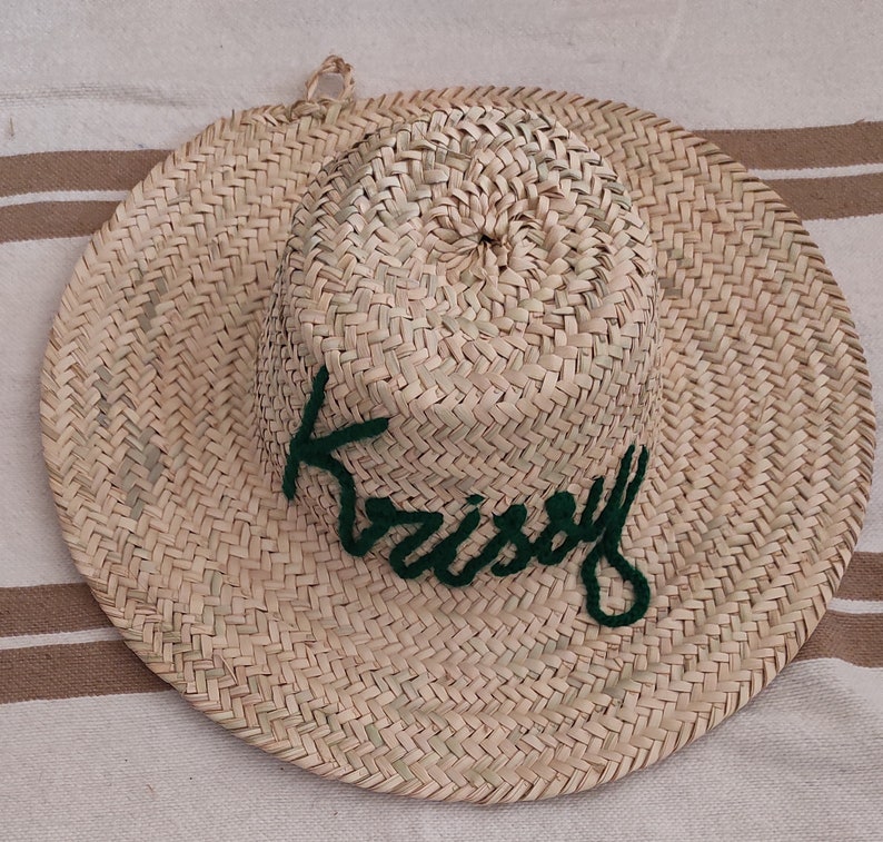 May include: A straw hat with a green embroidered word "Kristy" on the front.