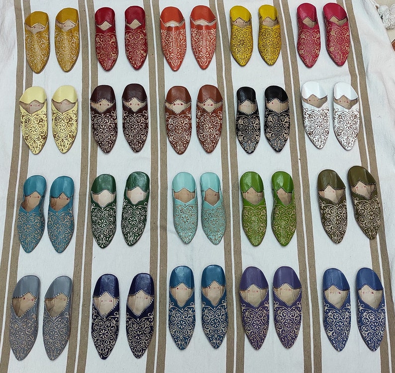 K&ouml;nnte beinhalten: Eine Sammlung von 24 Paar Lederschlappen in verschiedenen Farben, darunter Gelb, Rot, Braun, Blau, Gr&uuml;n, Wei&szlig; und Grau. Jeder Schlappen ist mit aufwendigen Blumenstickereien verziert.