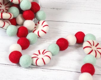 May include: A garland made of red, white, and green felt balls and peppermint candies. The garland is strung together with white thread and is perfect for decorating for the holidays.