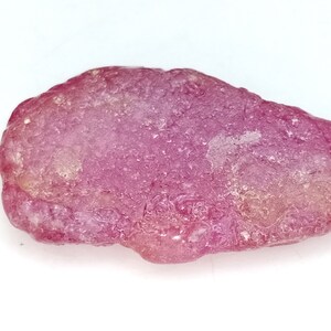 Könnte beinhalten: Ein roher, rosafarbener und leicht durchscheinender Edelstein mit einer natürlichen, unregelmäßigen Form.