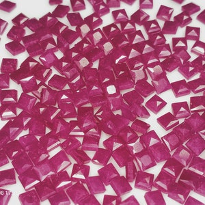 May include: A large quantity of small, square, pink, faceted rhinestones. The rhinestones have a pyramid-shaped top and a flat bottom.