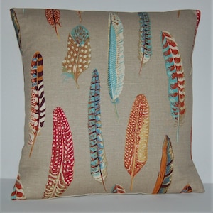 May include: Square decorative pillow with a beige background and a pattern of colorful feathers in shades of red, orange, blue, and brown. The feathers are of varying sizes and designs, creating a visually appealing textile.