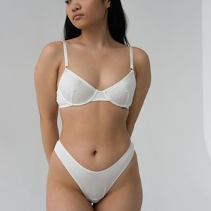 Pode incluir: Conjunto de roupa interior branca, um suti&atilde; e uma calcinha, com um design simples.