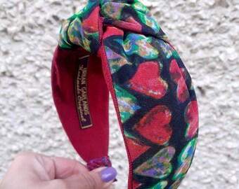 May include: A red headband with a knotted top and a black and green fabric with a heart pattern. The headband has the text "Urban Garlands Handmade Originals" on the side.