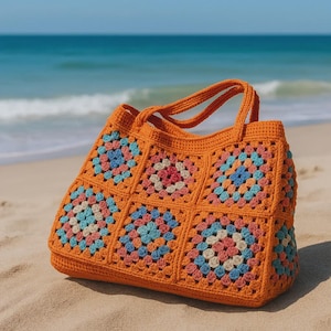 Puede incluir: Un bolso tote de crochet naranja con un dise&ntilde;o de cuadrados de la abuela. El bolso presenta cuadrados coloridos en tonos rosa, azul y crema. Tiene dos asas y est&aacute; sobre una playa de arena, con el oc&eacute;ano al fondo.