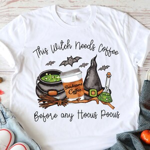 May include: White t-shirt with a black and green illustration of a witch's cauldron, a coffee cup with the text "Sanderson's Coffee", a witch's hat, and a potion bottle. The text "This Witch Needs Coffee Before Any Hocus Pocus" is printed on the shirt.