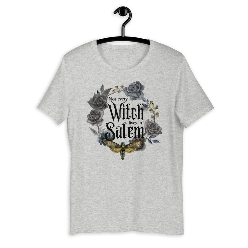 May include: Gray t-shirt with a black and white floral design and a moth. The text "Not every Witch lives in Salem" is printed on the shirt.