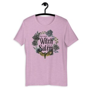 May include: A pink t-shirt with a black and gray floral wreath design. The wreath includes a moth and the text "Not every Witch lives in Salem".