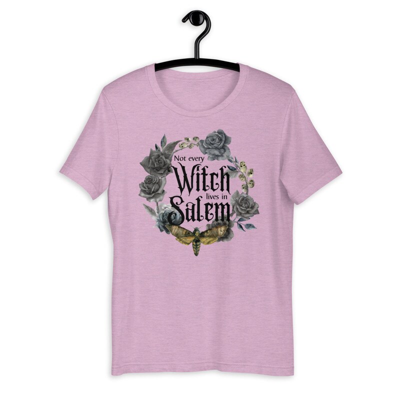 May include: A pink t-shirt with a black and gray floral wreath design. The wreath includes a moth and the text "Not every Witch lives in Salem".