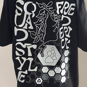 May include: Black t-shirt featuring white graphic text and illustrations. The design includes the words "Squad Style" and "Freedom" with a profile and a honeycomb pattern.