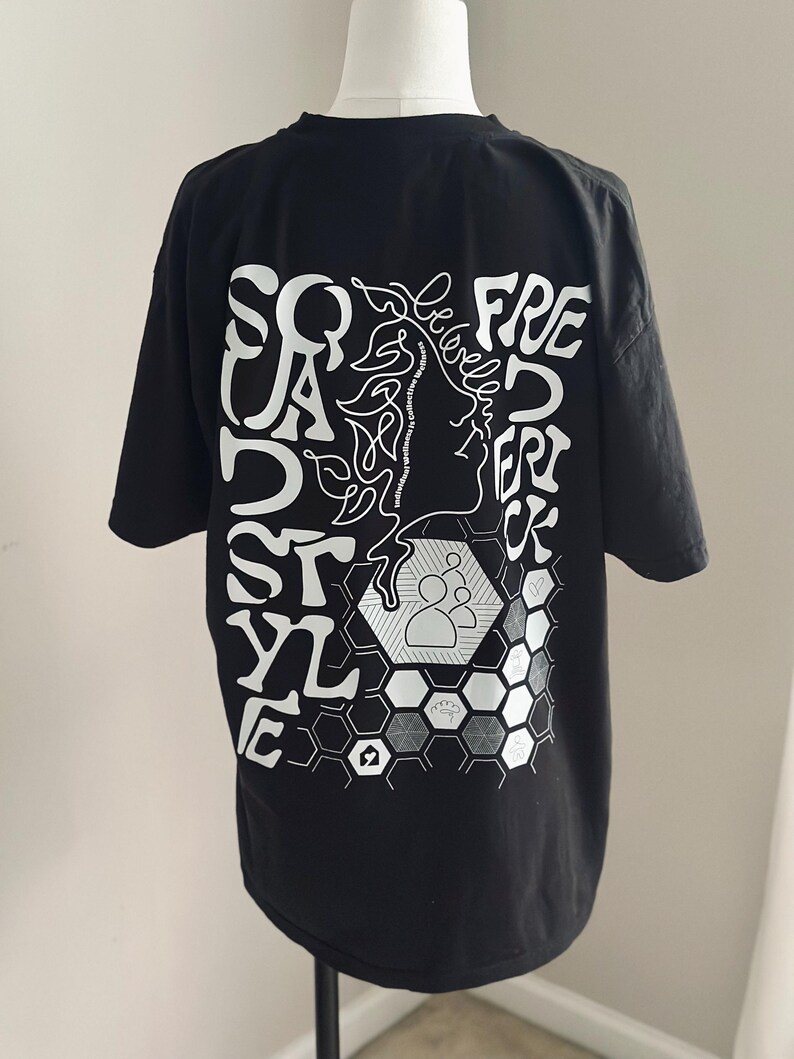 May include: Black t-shirt featuring white graphic text and illustrations. The design includes the words "Squad Style" and "Freedom" with a profile and a honeycomb pattern.