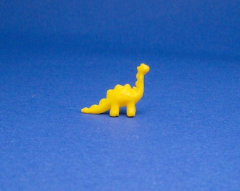 May include: A yellow plastic dinosaur toy with a long neck and a small tail. The dinosaur is standing on a blue surface.